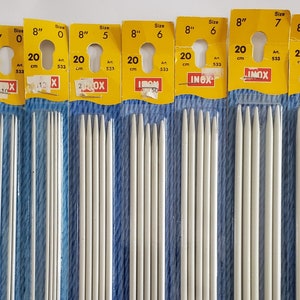 May include: Several packages of knitting needles are displayed, each with a yellow header indicating size and length. The needles are 8 inches long and come in various sizes, from 0 to 8. The packaging includes the measurement in centimeters.