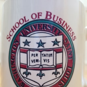 May include: White ceramic mug with the Washington University School of Business logo. The logo is a circular design with text and a crest featuring stars, an open book, and the words "PER TATEM VERI VIS". The mug also says "CENTURY CLUB".