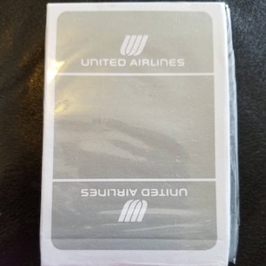 May include: A sealed deck of playing cards with the United Airlines logo and text. The cards are in a white box with a gray background and the United Airlines logo and text in white.
