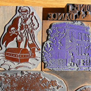 May include: A collection of vintage wood block printing stamps. The stamps feature designs of a pirate with a treasure chest, a building, and a building with palm trees. One stamp has the text "DINE AND DANCE".