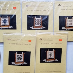 May include: Five packaged "A COUNTED CROSS STITCH KIT" sets. Each kit features a small, framed cross-stitch design in various geometric patterns. The kits are displayed on a white surface, with the brand name "Canterbury Designs, Inc." visible.