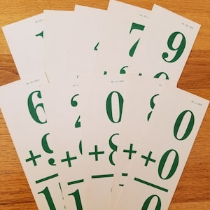 May include: A collection of white flashcards with green numbers and addition problems. The cards display single-digit addition problems, with answers. The cards are arranged in a fan shape on a wooden surface.