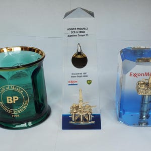 May include: An assortment of corporate awards and a mug. The green glass mug has a gold rim and the BP logo. A clear acrylic award features a gold oil rig model. A blue and clear acrylic award has an oil rig model.