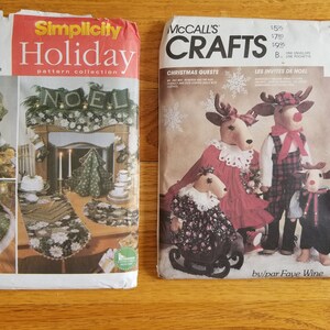 May include: Two vintage sewing pattern envelopes. The Simplicity pattern features holiday decor, including an angel tree topper and a table runner. The McCall's pattern shows Christmas reindeer dolls in various outfits.