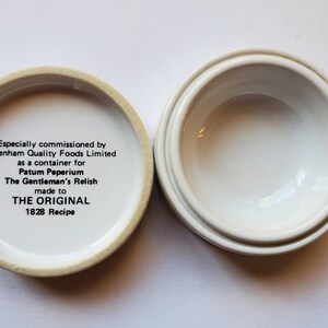 May include: Open, white ceramic container with a lid. The lid's interior features text: "Especially commissioned by Elsenham Quality Foods Limited...The Gentleman's Relish made to THE ORIGINAL 1828 Recipe."