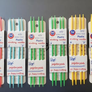 May include: A collection of Boye plastic knitting needles in various sizes and colors, including red, blue, green, and yellow. Each set is packaged with the "Boye" logo and the text "perfection points for happy knitting."