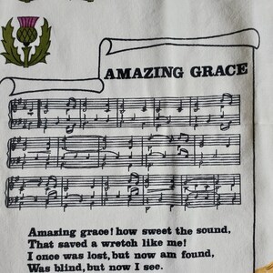 May include: White fabric featuring the text "AMAZING GRACE" above musical notation. The lyrics "Amazing grace! how sweet the sound, That saved a wretch like me!" are printed below the musical score. A thistle emblem is in the upper left corner.