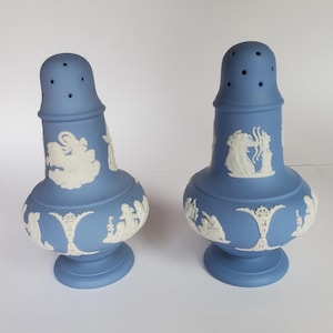 May include: Two blue ceramic salt and pepper shakers with white relief designs. The shakers have a bulbous base, a cylindrical body, and a perforated top. The white relief depicts classical figures and scenes.