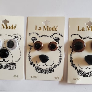 May include: Three packages of La Mode brand craft supplies. Each package features a bear face illustration with different styles of plastic eyes and a black nose. The packages are labeled with prices and product numbers.