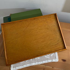 May include: A rectangular wooden serving tray with a smooth, light brown finish and a thin, raised border frame. The tray features a visible wood grain pattern across its flat surface, showcasing a natural, warm-toned appearance throughout.