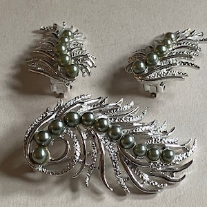May include: A set of three silver tone earrings with a feather design and green faux pearls. The earrings are clip-on style.