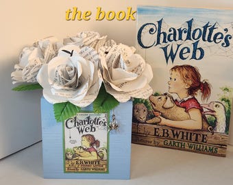 May include: A light blue wooden box featuring a Charlotte's Web book cover illustration, filled with paper roses crafted from book pages and green leaves. A small silver spider charm hangs from the box next to a copy of the book Charlotte's Web.