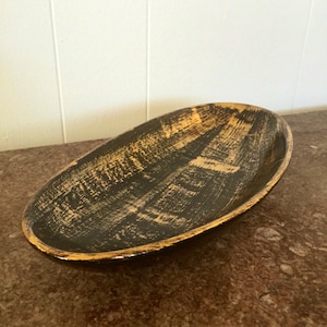 May include: An oval-shaped ceramic serving dish with a black and gold glaze. The dish has a rustic, hand-painted look.