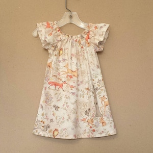 May include: A white dress with a forest animal print. The dress has a gathered neckline and short, ruffled sleeves.