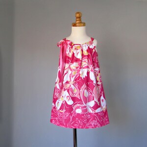 May include: A sleeveless pink dress with a floral pattern in white, yellow, and pink. The dress has a ribbon tie on the shoulder and a darker pink hemline with a floral design. The dress is displayed on a mannequin.