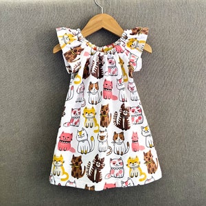 May include: A white dress with a ruffled neckline and short sleeves. The dress is covered in a pattern of colourful cats.