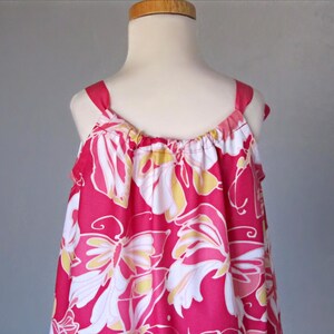 May include: A sleeveless, pink dress with a floral pattern. The dress features white, yellow, and pink flowers. The straps are pink and the dress is displayed on a mannequin.