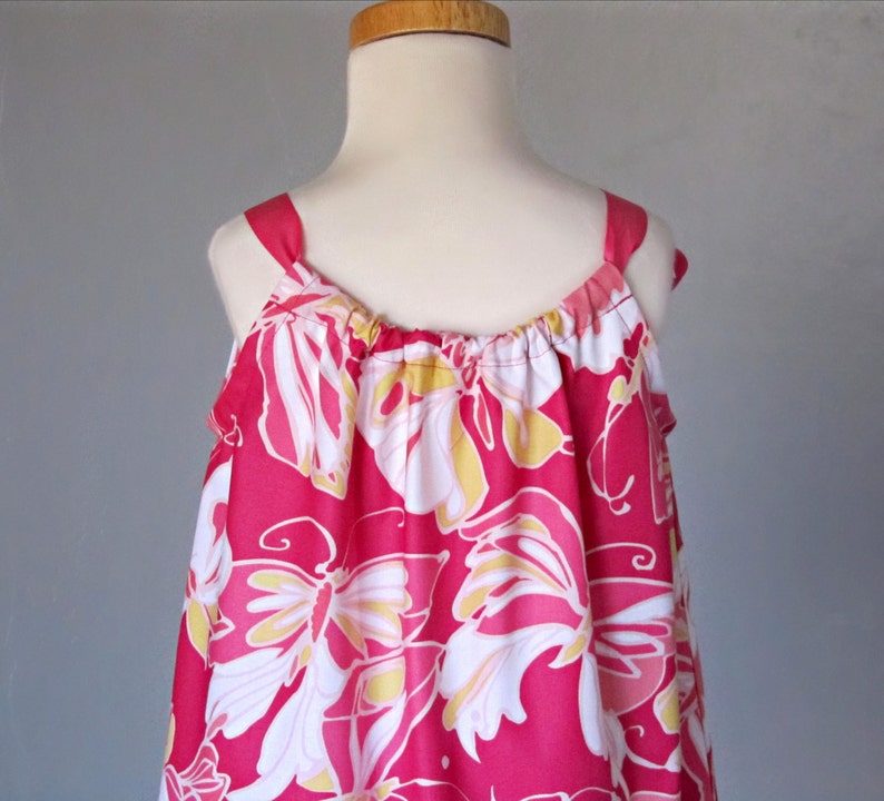 May include: A sleeveless, pink dress with a floral pattern. The dress features white, yellow, and pink flowers. The straps are pink and the dress is displayed on a mannequin.
