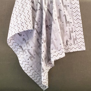 May include: A white baby blanket with a gray chevron border and a pattern of gray giraffes on a white background.
