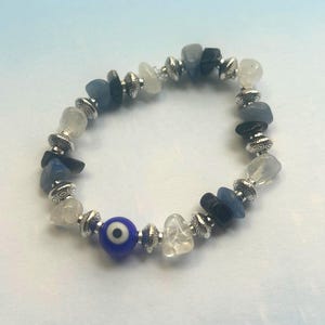 Könnte beinhalten: Ein blaues und weißes böses Auge-Charm-Armband mit silbernen Perlen und blauen und weißen Steinen.