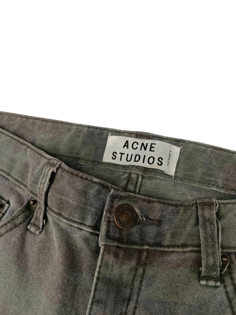 Puede incluir: Primer plano de unos vaqueros con estampado de camuflaje. Los vaqueros tienen cierre de bot&oacute;n y trabillas para el cintur&oacute;n. Se ve una etiqueta blanca con el texto "ACNE STUDIOS".