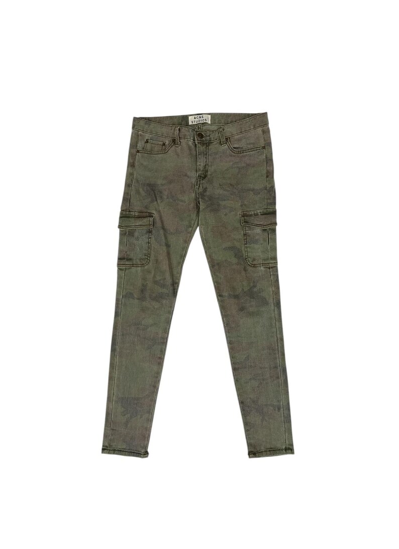 Puede incluir: Pantalones cargo de camuflaje verde con dos bolsillos laterales. Los pantalones tienen un corte ajustado y cierre de bot&oacute;n y cremallera. La marca "ACNE STUDIOS" es visible en la cintura.
