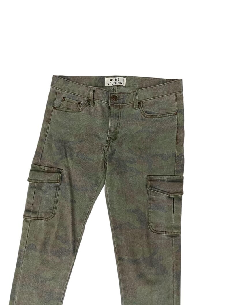 Puede incluir: Pantalones cargo de camuflaje verde con la etiqueta "ACNE STUDIOS". Los pantalones tienen dos bolsillos cargo en las piernas y bolsillos delanteros y traseros est&aacute;ndar. Los pantalones est&aacute;n hechos de una tela duradera.