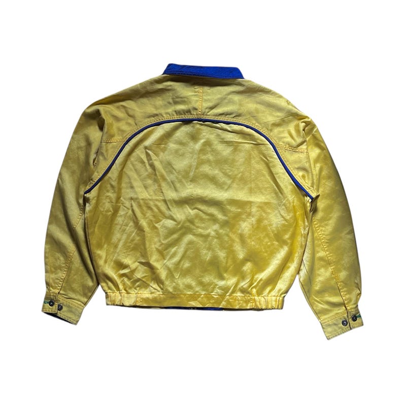 May include: A yellow jacket with a blue collar and blue trim. The jacket has a zipper closure and a drawstring waist.