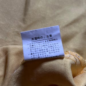 May include: A white tag with black text on a yellow fabric background. The tag contains instructions for washing the fabric. The text reads: "Washing Instructions: Do not leave wet for long periods of time. Do not use bleach. Do not tumble dry. Wash separately."