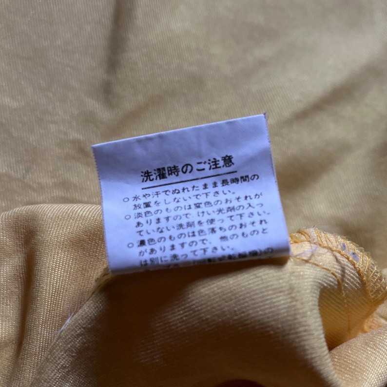 May include: A white tag with black text on a yellow fabric background. The tag contains instructions for washing the fabric. The text reads: "Washing Instructions: Do not leave wet for long periods of time. Do not use bleach. Do not tumble dry. Wash separately."