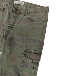 Puede incluir: Pantalones con estampado de camuflaje en tonos verdes, marrones y grises. Los pantalones tienen un bolsillo cargo y la etiqueta de la marca "ACNE STUDIOS". Tienen cierre de bot&oacute;n y cremallera, adem&aacute;s de bolsillos est&aacute;ndar.