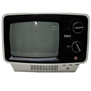 May include: A vintage RCA television set with a white and black color scheme. The small TV has a rectangular screen, two control knobs, and the RCA logo. The base has a series of horizontal vents.