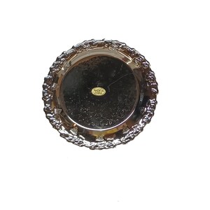 May include: Silver-colored round serving tray with a decorative embossed border. The tray has a label that reads "Made in China".