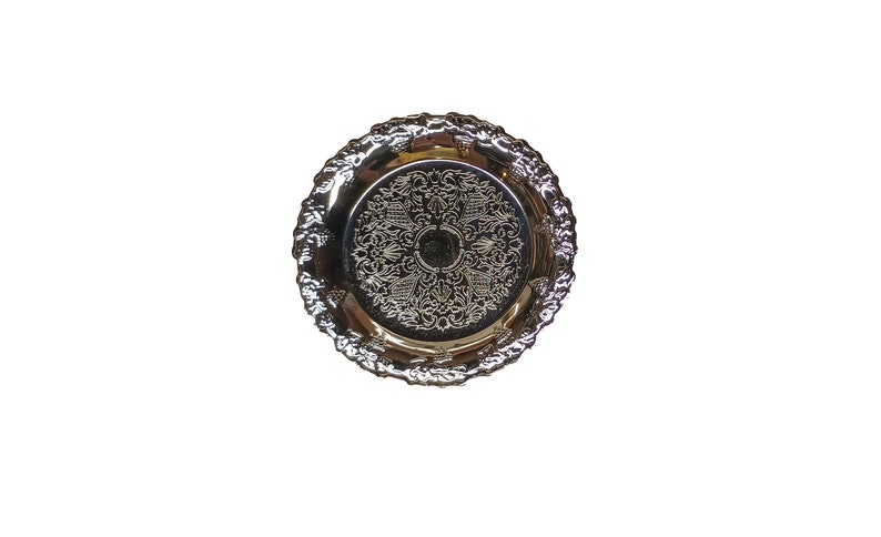 May include: A silver decorative tray with an ornate design. The tray has a raised rim and a smooth surface.