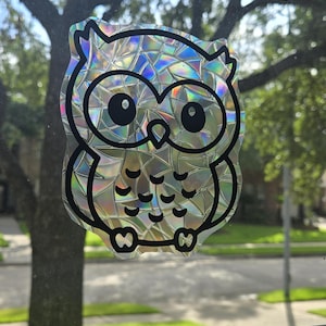 May include: A holographic owl sticker with a black outline. The owl has large eyes and a detailed design.