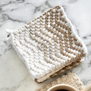 May include: Two woven beige and white pot holders with a cup of coffee on one of the holders.