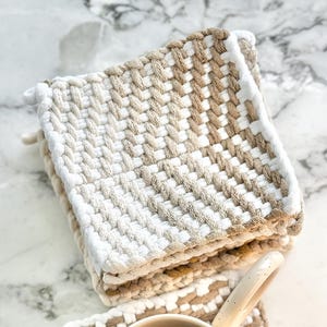 May include: A white and beige woven coaster with a white ceramic mug filled with black coffee on top. The coaster is made of a woven material and has a square shape.