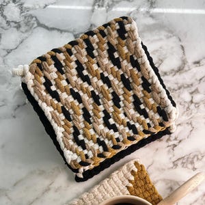 May include: Two woven cotton coasters in black, white, and mustard yellow. A white ceramic mug with black coffee sits on top of one of the coasters.