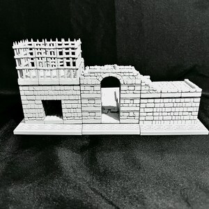 Puede incluir: Un modelo de castillo en miniatura gris con una torre, un arco y una base rectangular. El castillo presenta un dise&ntilde;o detallado de ladrillos y una estructura de estilo madera en la parte superior de la torre. Modelo para juegos de mesa o exhibici&oacute;n.