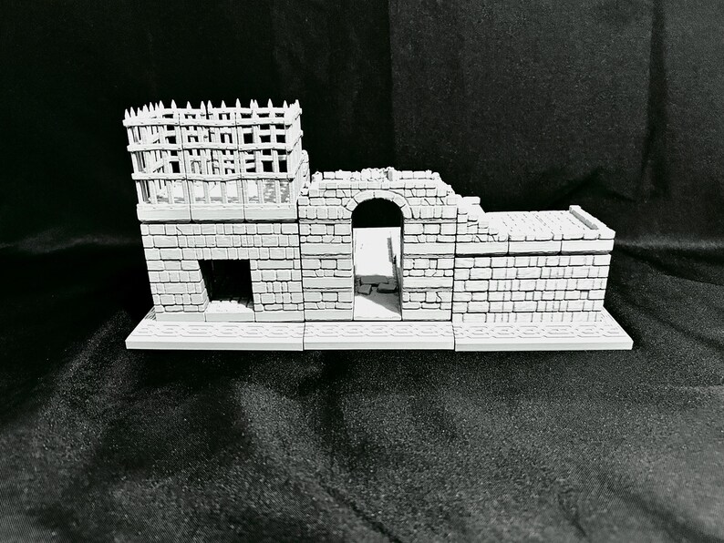 Puede incluir: Un modelo de castillo en miniatura gris con una torre, un arco y una base rectangular. El castillo presenta un dise&ntilde;o detallado de ladrillos y una estructura de estilo madera en la parte superior de la torre. Modelo para juegos de mesa o exhibici&oacute;n.