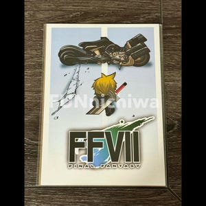 May include: A white card with a blue, green, and black graphic of the Final Fantasy VII logo. The logo is surrounded by a green and blue swirl. A cartoon character with blonde hair and a sword is standing on a cracked surface. A black motorcycle is flying in the air above the character.