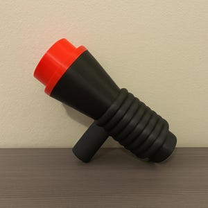 May include: A 3D-printed megaphone in black, red, and grey. The megaphone has a flared, cone-shaped body with a red rim at the top. The handle and the ribbed section are grey.