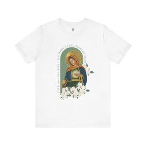 May include: White t-shirt with a graphic of the Immaculate Heart of Mary. The graphic features a painting of Mary holding a heart with a crown of thorns. The text "The Flame of Love of the Immaculate Heart of Mary" surrounds the image.