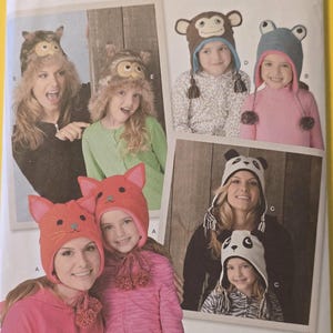 May include: Simplicity sewing pattern featuring animal-themed hats. The pattern includes designs for an owl, monkey, frog, panda, and cat hats. The cover shows photos of the hats being worn by adults and children.