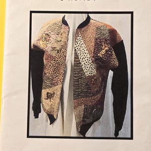 May include: A Crazy Patch Sweatshirt Jacket is displayed in a framed image. The jacket features a patchwork design with various textures and patterns in shades of brown, beige, and black. The sleeves are solid black, and the jacket is open, revealing a white background.