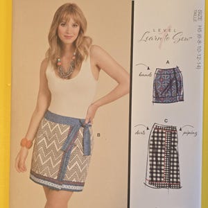 May include: McCall's sewing pattern M8409. The pattern features a woman wearing a wrap skirt with a chevron pattern and a blue and white border. The pattern includes illustrations of skirt designs and the text "Learn to Sew".