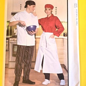 May include: McCall's sewing pattern M8332 for culinary apparel. The envelope features illustrations of a short-sleeve white chef coat, long-sleeve red chef coat, striped pants, a white apron, and two styles of chef hats in sizes S-M-L-XL-XXL.