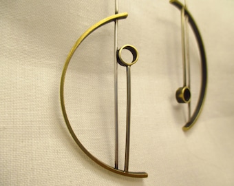 Könnte beinhalten: Ein Paar Ohrringe aus Gold und Silber mit geometrischem Design. Die Ohrringe bestehen aus zwei dünnen Metallstäben, die durch ein gebogenes Metallstück verbunden sind. Das gebogene Metallstück ist halbkreisförmig.