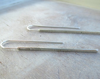 Könnte beinhalten: Ein Paar silberne Ohrringe mit einem strukturierten Balken-Design. Die Ohrringe sind schlicht und modern.