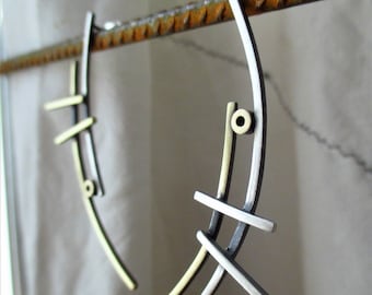 May include: A pair of silver and gold earrings with a geometric design. The earrings are made of metal and have a curved shape.